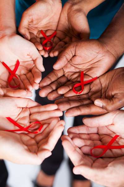 Multiracial hands holding red HIV ribbon in their palms